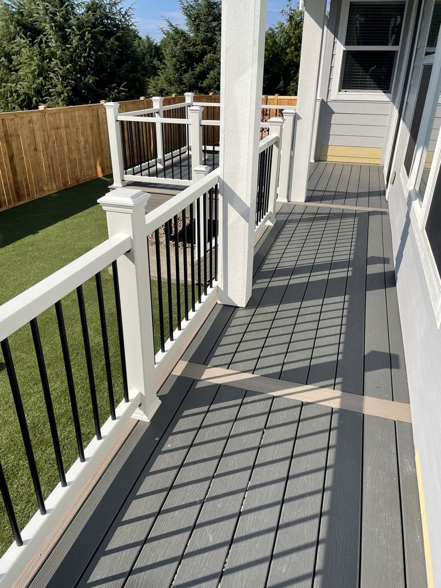 Long composite porch with white and black railing overlooking a fenced backyard