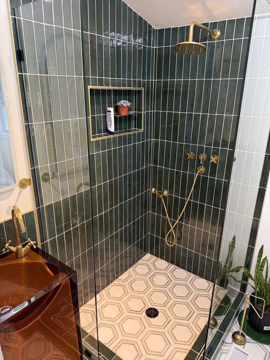 Walk-in shower with green vertical tile, brass fixtures, and hexagon mosaic floor